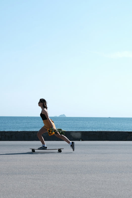 A woman riding a skateboard down a street next to the ocean